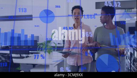 Marchant des femmes occasionnelles discutant des données en direct au bureau, avec des tablettes et des graphiques holographiques Banque D'Images