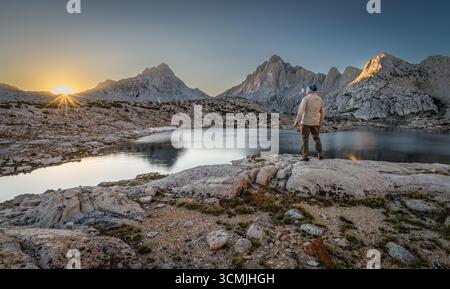 Vue arrière d'un homme debout sur un rocher devant le lac Grinnell à l'aube regardant les montagnes de la Sierra Nevada, Sierra National Forest, Californie, États-Unis Banque D'Images