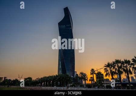 Vue d'un gratte-ciel moderne à Koweït City au coucher du soleil avec des palmiers silhouettés au premier plan au parc Al Shaheed. Koweït City, Koweït. Banque D'Images