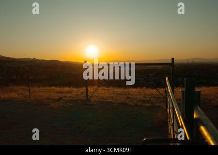 Coucher de soleil doré sur les collines d'Antioch, Californie, avec une clôture rustique et des barbelés au premier plan. Prise près de Contra Loma et East Bay Banque D'Images