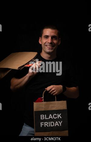 Homme souriant montrant des sacs à provisions avec inscription du vendredi noir sur fond sombre Banque D'Images