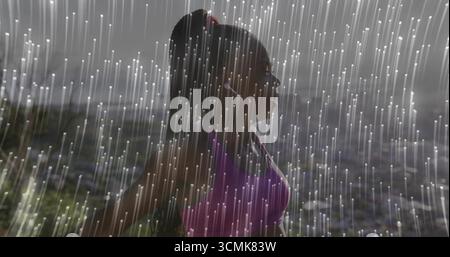 Coureur noir debout portant un soutien-gorge de sport violet et des écouteurs blancs à flanc de colline, avec des stries de pluie Banque D'Images