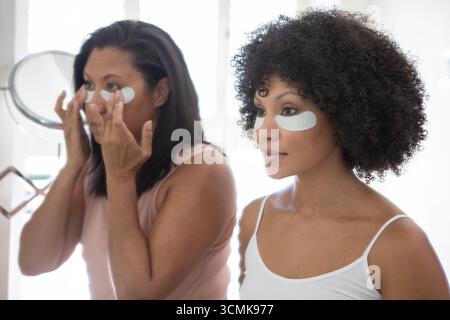 Mère et fille debout à la vanité en appliquant des patchs de gel sous les yeux à l'aide d'un miroir de table Banque D'Images