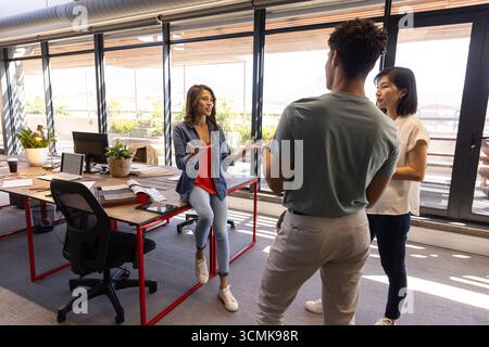 Divers collègues discutent des idées de projet autour d'un bureau en bois à cadre rouge dans le bureau Banque D'Images
