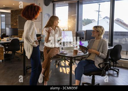 Diverses collègues féminines se réunissant autour du bureau dans le bureau avec des ordinateurs portables et des tasses à café Banque D'Images