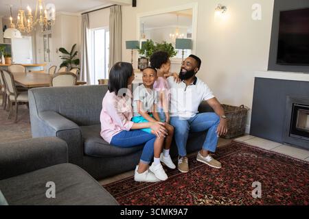Famille diverse assis ensemble sur un canapé gris sur tapis rouge à motifs dans le salon lumineux Banque D'Images