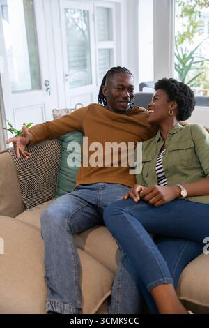 Couple afro-américain se penchant l'un vers l'autre et conversant sur le canapé dans le salon Banque D'Images