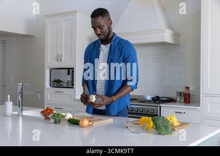 Homme afro-américain dans les années trente tranchant l'oignon avec le couteau de chef sur la planche à découper à la cuisine Banque D'Images
