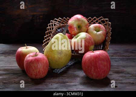 Pommes rouges mûres dans un panier avec une poire mûre sur une table en bois Banque D'Images