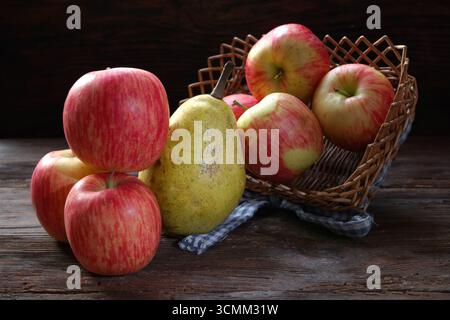 Pommes rouges mûres dans un panier avec une poire mûre sur une table en bois Banque D'Images