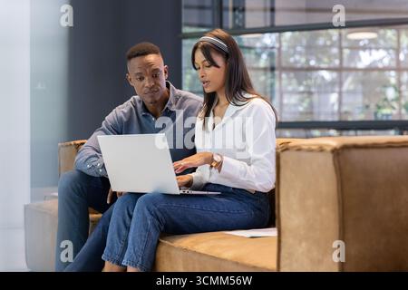 Divers collègues examinant le papier, tapant sur un ordinateur portable assis dans le salon de bureau sur un canapé en cuir Banque D'Images