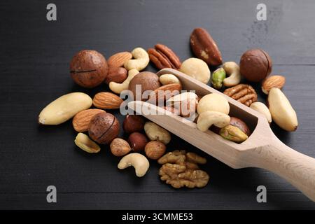 Mélange de différentes noix et cuillère sur la table en bois noir, gros plan Banque D'Images