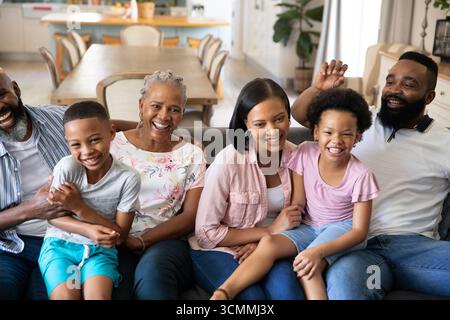 Famille multigénérationnelle diversifiée assise sur un canapé gris dans le salon, riant et interagissant Banque D'Images