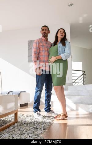 Couple diversifié debout dans le couloir avec une femme enceinte portant une robe verte près de l'escalier et de l'art. Banque D'Images