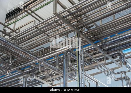 Vue aérienne de tuyaux en acier inoxydable montés au plafond dans une installation de production alimentaire moderne, mettant en valeur une infrastructure industrielle complexe Banque D'Images