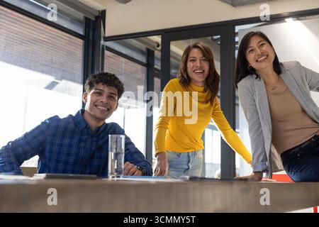 Divers collègues se penchant autour d'une table de conférence en bois dans la salle de conférence et examinant le bloc-notes Banque D'Images