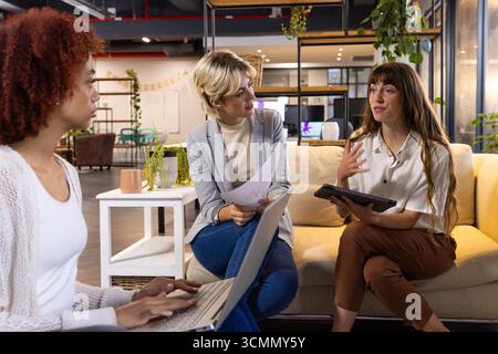 Diverses collègues féminines se réunissant dans le salon de bureau tout en examinant des graphiques imprimés, tablette Banque D'Images