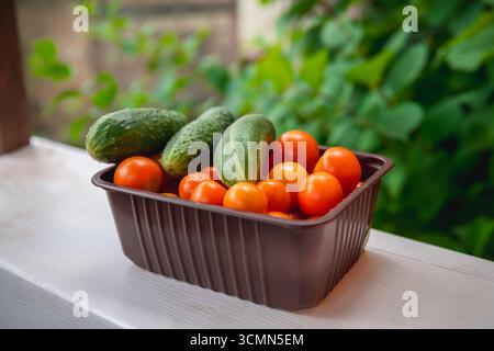 Les concombres fraîchement cueillis et les tomates cerises sont nichés ensemble dans un récipient en plastique brun, mettant en valeur les couleurs et les textures vibrantes d'une santé Banque D'Images