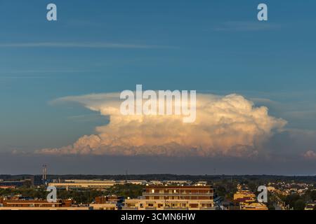 Un superbe paysage urbain capturé à l'aube, avec une spectaculaire formation de nuages dorés illuminée par le soleil levant. L'image met en valeur une ville dynamique Banque D'Images
