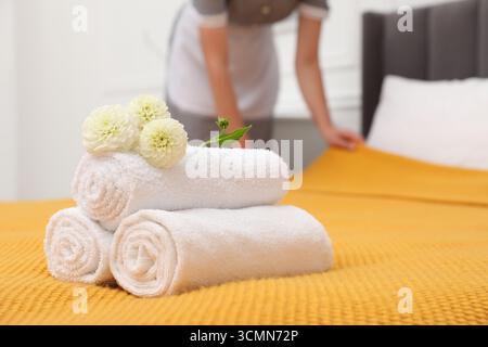 Femme de chambre travaillant dans la chambre d'hôtel, se concentrer sur les serviettes éponges roulées et les fleurs de dahlia sur le lit Banque D'Images