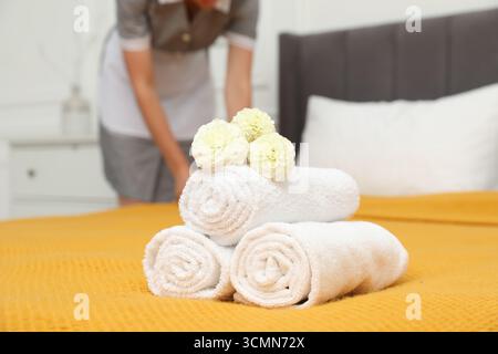 Femme de chambre travaillant dans la chambre d'hôtel, se concentrer sur les serviettes éponges roulées et les fleurs de dahlia sur le lit Banque D'Images