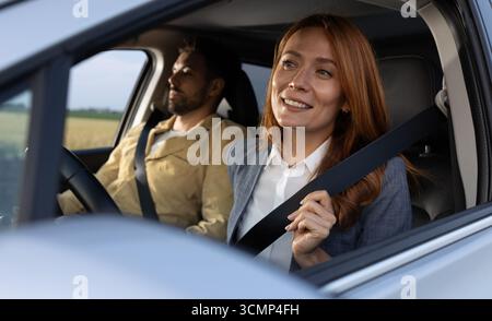 Femme joyeuse bouclant sa ceinture de sécurité avant d'essayer de conduire sa nouvelle voiture de luxe avec un ami dans le siège passager Banque D'Images