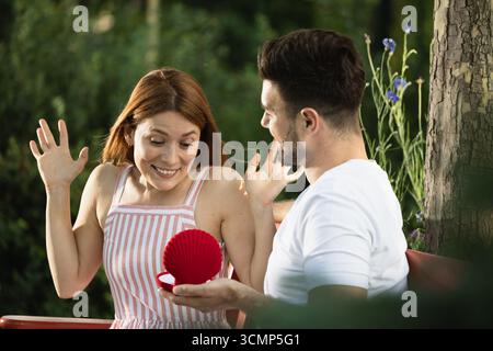 Jolie femme se faisant proposer par son petit ami dans le parc, choquée et joyeuse expression sur son visage quand elle voit la bague Banque D'Images
