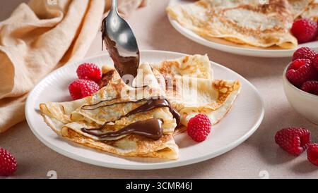 assiette de crêpes fraîchement cuites décorée de framboises. cuire en versant la sauce au chocolat fondu sur les crêpes pour faire un délicieux petit déjeuner, desser sucré Banque D'Images