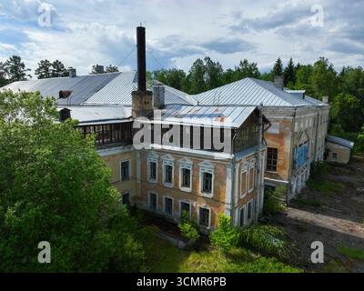 Une vue aérienne rapprochée de l'ancien sanatorium Andreevskoe, montrant sa façade en ruine et un bâtiment adjacent de style industriel avec une grande cheminée. Banque D'Images