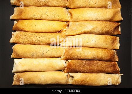 Crêpes frites et roulées empilées côte à côte sur une surface sombre, vue de dessus, gros plan Banque D'Images
