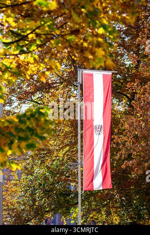 Le drapeau national autrichien avec les armoiries est accroché à un poteau sur fond d'arbres d'automne. Fête nationale autrichienne. Jour de l'indépendance Banque D'Images