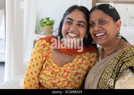 Mère indienne portant saree et fille dans salwar kameez souriant tout en étant assis sur le canapé à la maison Banque D'Images
