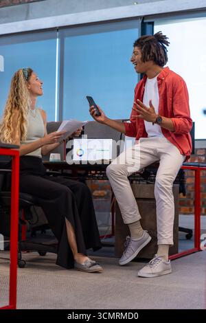 Divers collègues discutent des résultats de données sur ordinateur portable dans un espace de travail moderne avec des rapports imprimés Banque D'Images