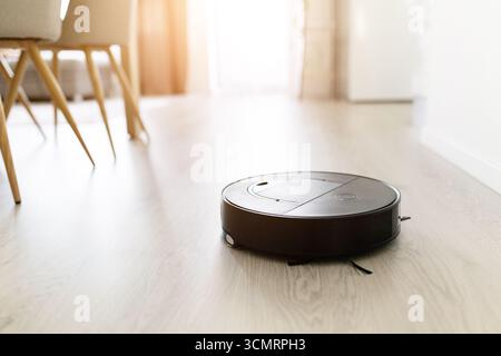 Aspirateur robotisé travaillant sur plancher en bois dans une maison moderne lumineuse Banque D'Images