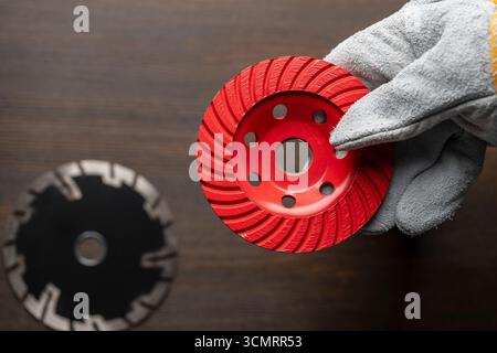Main d'ouvrier dans des gants de construction tenant le nouveau disque diamant rouge pour meuler le béton, gros plan, espace de copie Banque D'Images