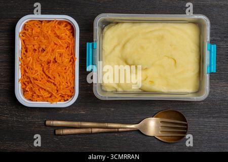 Plusieurs plats dans des boîtes en plastique pour le petit déjeuner sur une table en bois, gros plan, vue de dessus. Purée de pommes de terre et carottes râpées dans des récipients alimentaires en plastique Banque D'Images