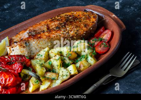 Savoureux poisson de saumon cuit au four avec poivron rouge, pomme de terre, tomate et citron dans un plat en argile sur la table, gros plan, Banque D'Images