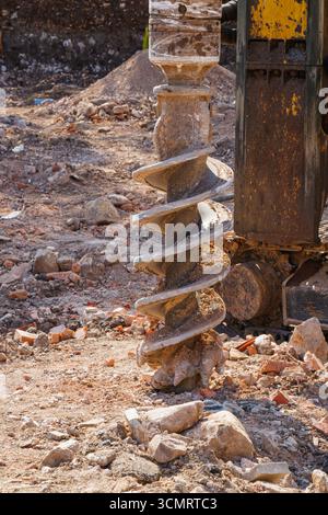 Gros plan d'une foreuse à tarière extra-robuste recouverte de sol et de roches sur un chantier de construction, utilisée pour le forage de fondations et les travaux d'excavation dans l'industrie Banque D'Images