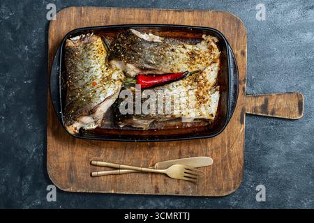 Filet de carpe cuit au four avec piment rouge et épices dans un plat de cuisson en verre sur une planche à découper, gros plan, vue de dessus Banque D'Images