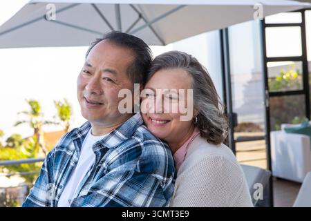 Couple divers serrant sur la terrasse causeuse sous parasol donnant sur le jardin Banque D'Images