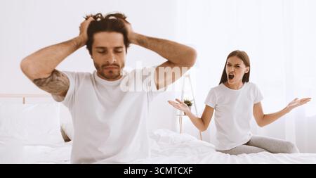 Triste mari européen millénaire avec le chaume est assis sur le lit et tient la tête avec la main, la femme se gonfle et hurle à Guy Banque D'Images