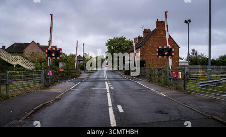 Chemin de fer goudronné vide traversant des routes avec des barrières fermées et des feux clignotants avertissant les conducteurs de l'approche d'un train par temps nuageux Banque D'Images