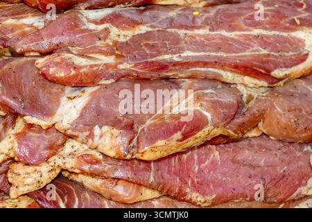 Gros plan de tranches de porc cru marinées avec de l'assaisonnement et des herbes, empilées ensemble comme un fond de texture de viande prêt à griller ou à cuire. Banque D'Images