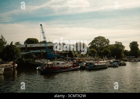 Twickenham, Londres, Royaume-Uni – 2025.09.06 – vue d’un chantier naval sur la Tamise avec une grande grue bleue, des bateaux amarrés et des bâtiments au bord de la rivière entourés Banque D'Images