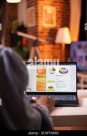 Gros plan de femme afro-américaine tapant sur ordinateur portable tout en travaillant à distance au coucher du soleil. Productif femme freelance gère les tâches de la maison dans un salon confortable, axé sur les objectifs de l'entreprise. Banque D'Images