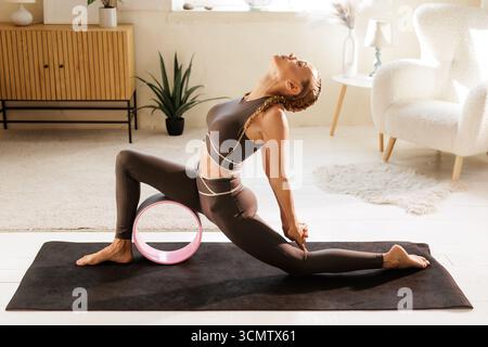 Femme en fente profonde dos en utilisant une roue de yoga pour ouvrir les hanches et la poitrine améliorer la mobilité de la colonne vertébrale et la posture à la maison Banque D'Images