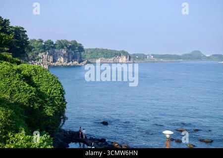 Une vue large depuis Jaguri culture & Arts Park montre des promontoires de basalte et des criques calmes, avec des visiteurs debout sur les rochers de marée le long de la côte de Seogwipo. Banque D'Images