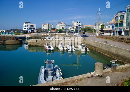 Une vue plus large du port de Namwon montre des bateaux de pêche bordés, des grues de quai et des points de carburant autour du bassin du port, avec des appartements de faible hauteur et des magasins faisant face Banque D'Images