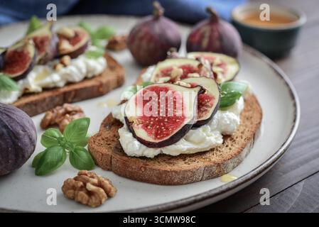 Sandwichs aux figues, fromage à la crème, basilic et miel sur assiette sur fond de bois, gros plan Banque D'Images