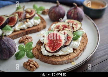 Sandwichs aux figues, fromage à la crème, basilic et miel sur assiette sur fond de bois, gros plan Banque D'Images